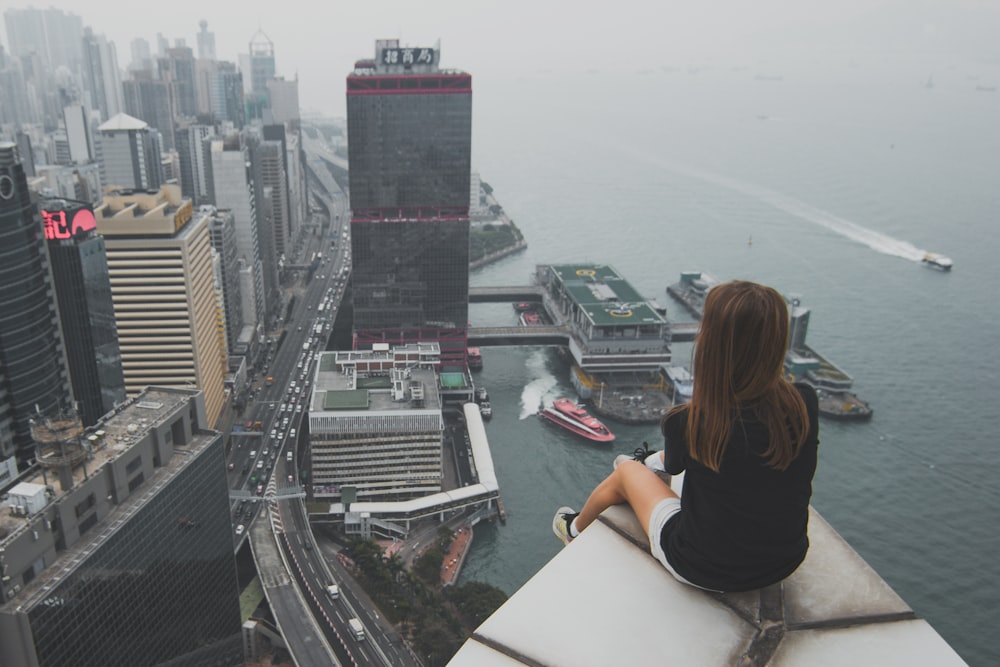 Mujer sentada en la parte superior del edificio con vistas a la ciudad por la bahía durante el día