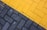 A close-up view of a paved surface with interlocking bricks. The bricks are arranged in two distinct sections; one side is painted yellow and the other is gray, creating a diagonal division.