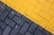 A close-up view of a paved surface with interlocking bricks. The bricks are arranged in two distinct sections; one side is painted yellow and the other is gray, creating a diagonal division.