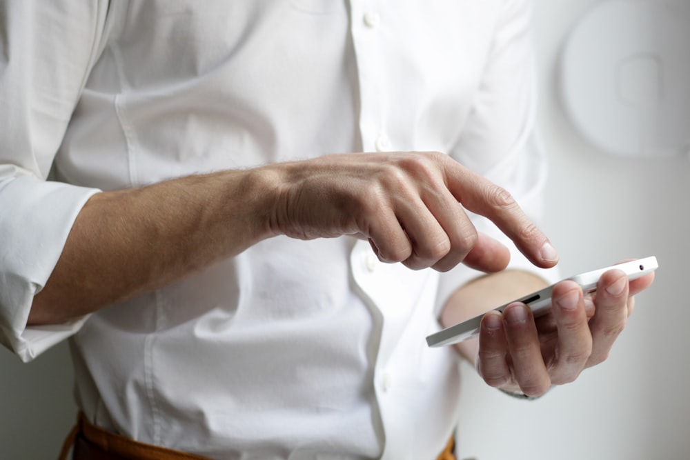 personne tenant un smartphone Android blanc en chemise blanche