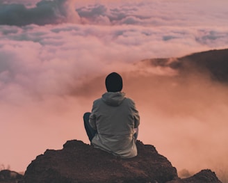 man sitting on cliff looking at the clouds