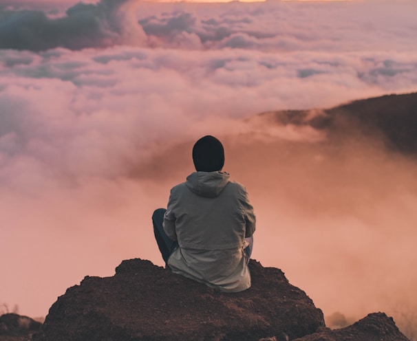man sitting on cliff looking at the clouds