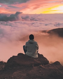 man sitting on cliff looking at the clouds
