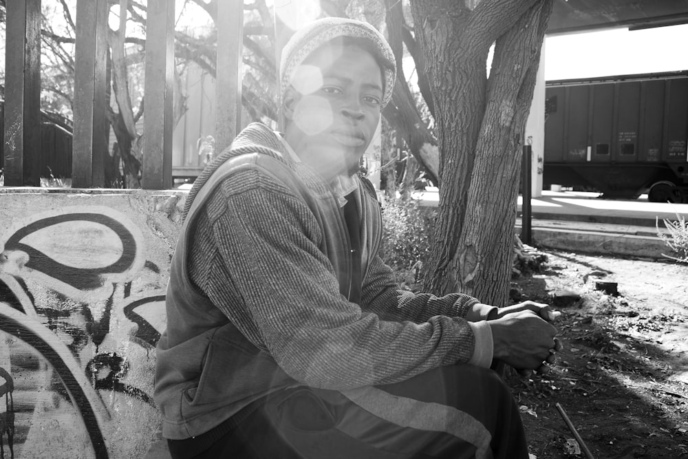 grayscale photography of woman sitting beside tree