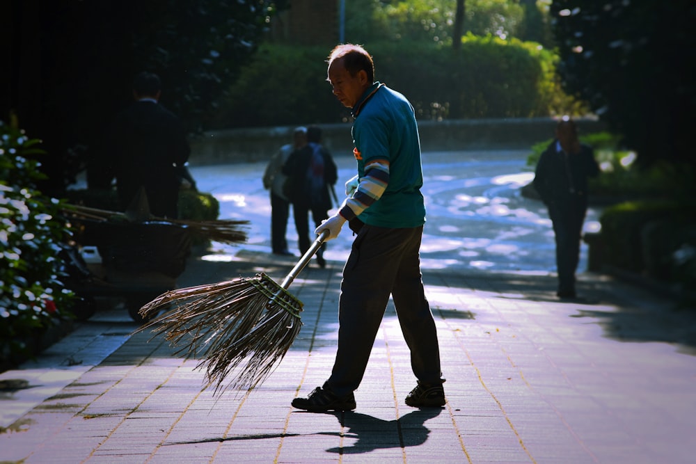 Homem segurando vassoura varrendo na calçada