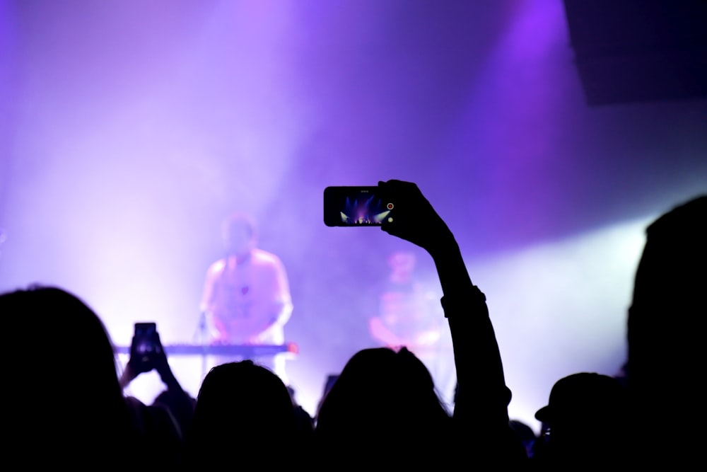 photography of person holding smartphone capture video during concert