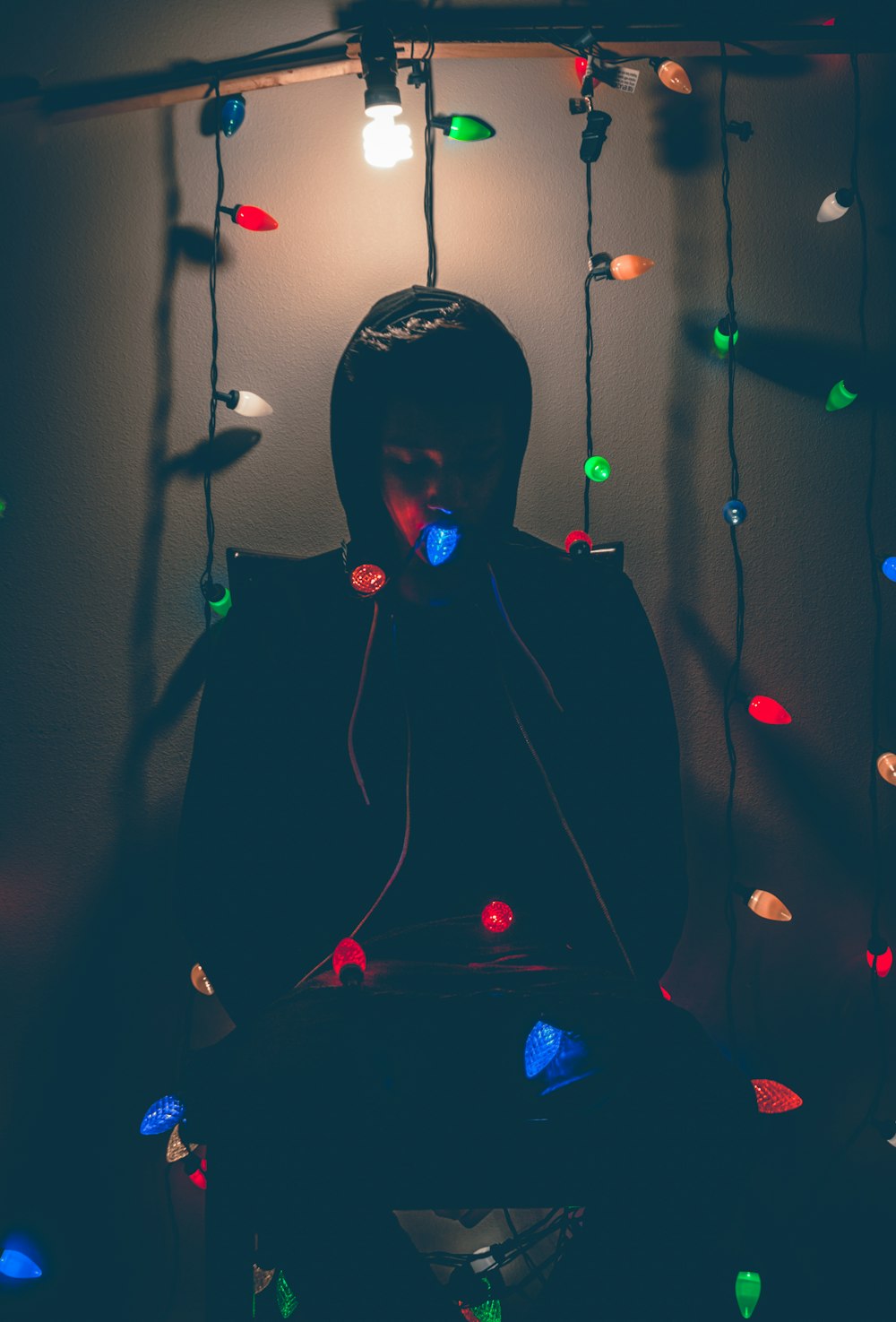 man sitting while biting multicolored string lights