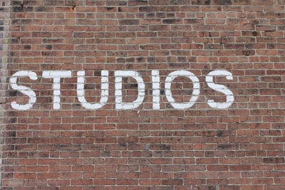 Large white letters spelling 'STUDIOS' are painted on a textured red brick wall, with the bricks arranged in a standard horizontal pattern.