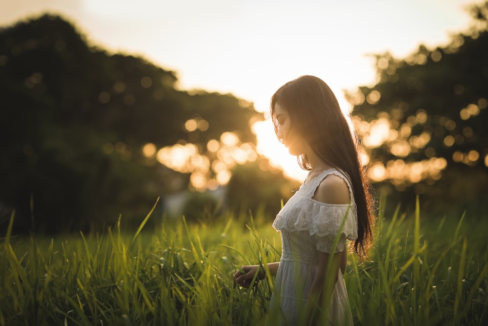 Fotografia de foco raso da mulher em pé no campo da grama enquanto segura a grama