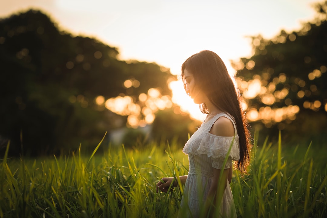 fotografia a fuoco superficiale di una donna in piedi su un campo di erba mentre tiene dell'erba