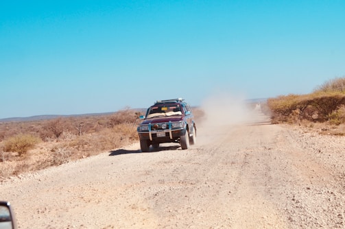 A vehicle driving along a dirt road near empty land.