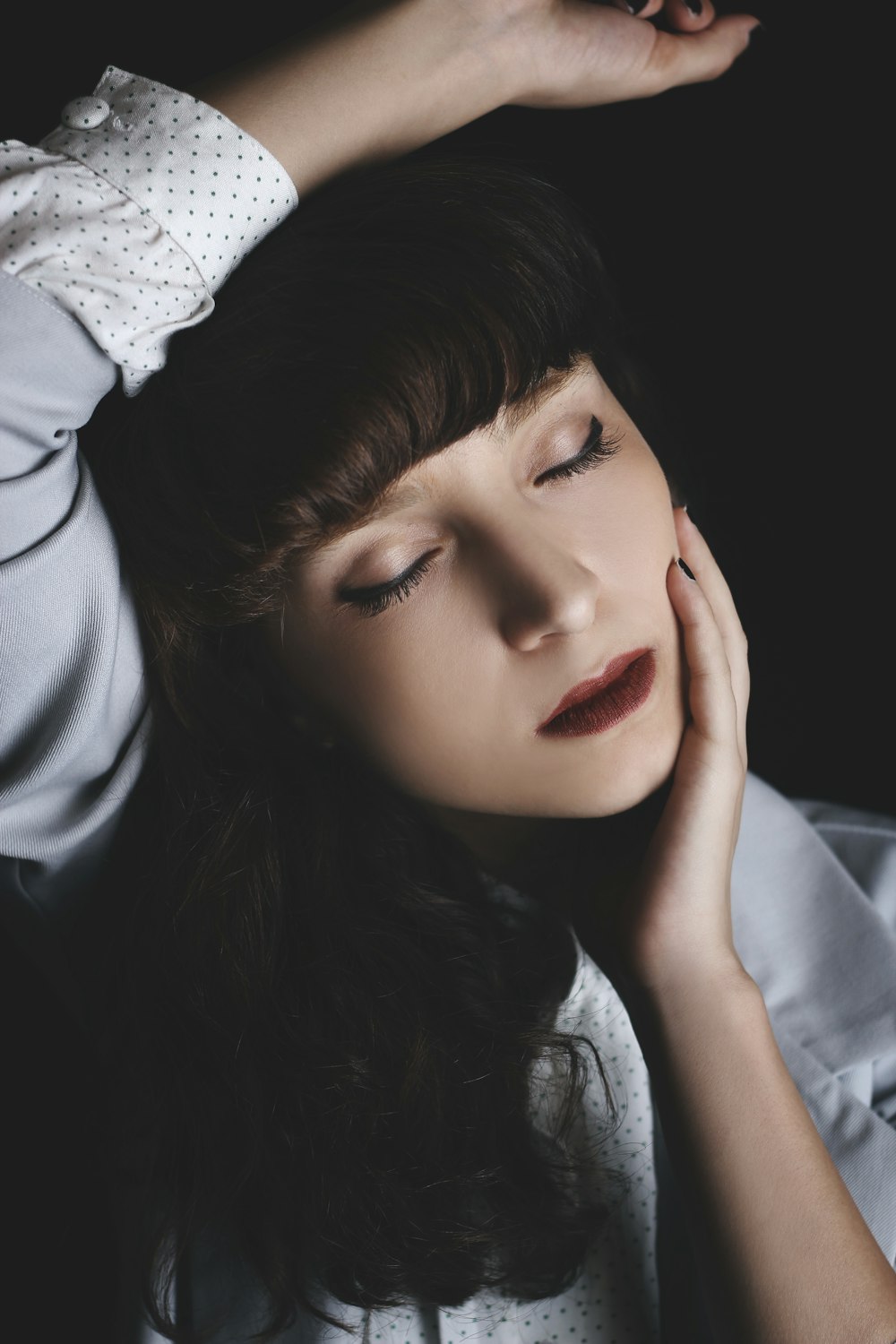 woman holding her cheek while rising her right hand in black background