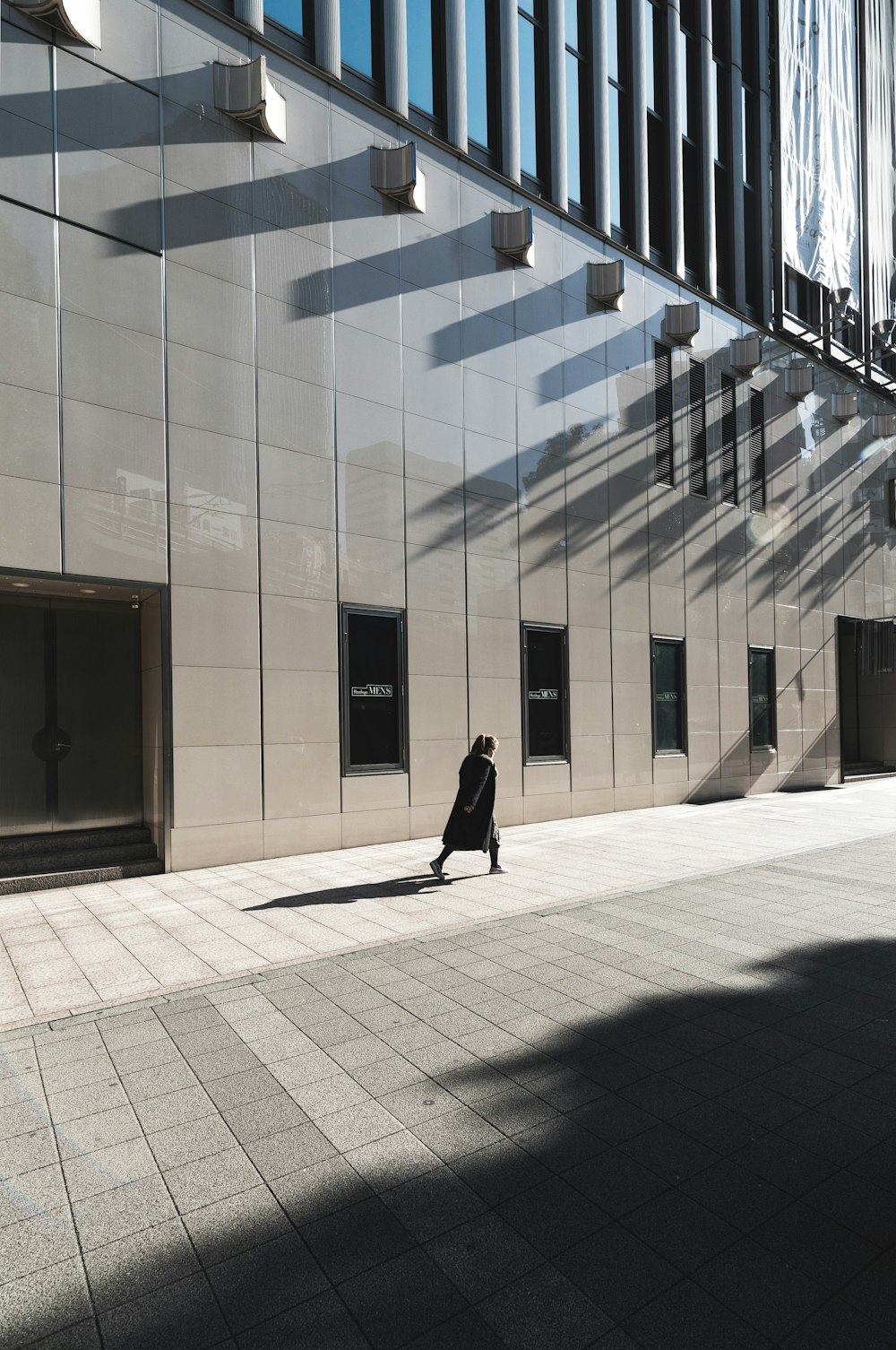 Frau im schwarzen langärmeligen Kleid geht neben dem Gebäude