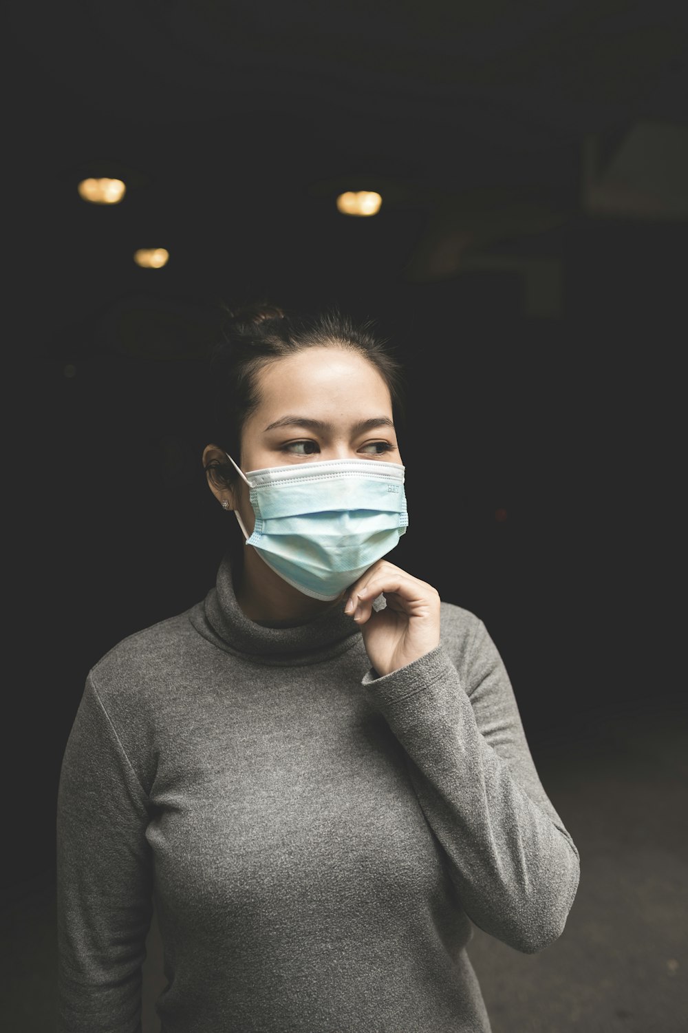 Femme portant un masque turquoise et une chemise à col roulé grise