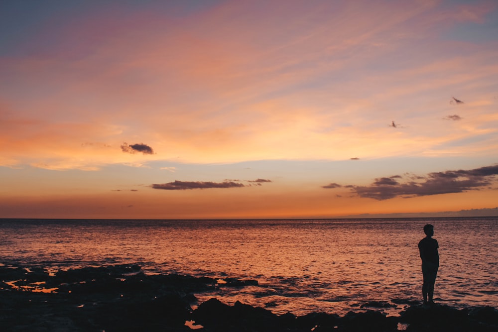 silhouette of man standing on rock facing body of water