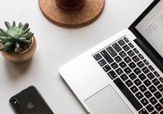 space gray iPhone X beside turned on laptop beside coffee and succulent plant