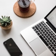 space gray iPhone X beside turned on laptop beside coffee and succulent plant