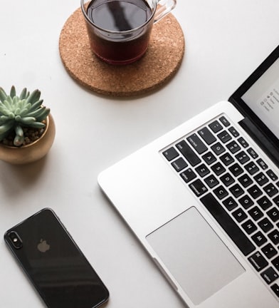 space gray iPhone X beside turned on laptop beside coffee and succulent plant