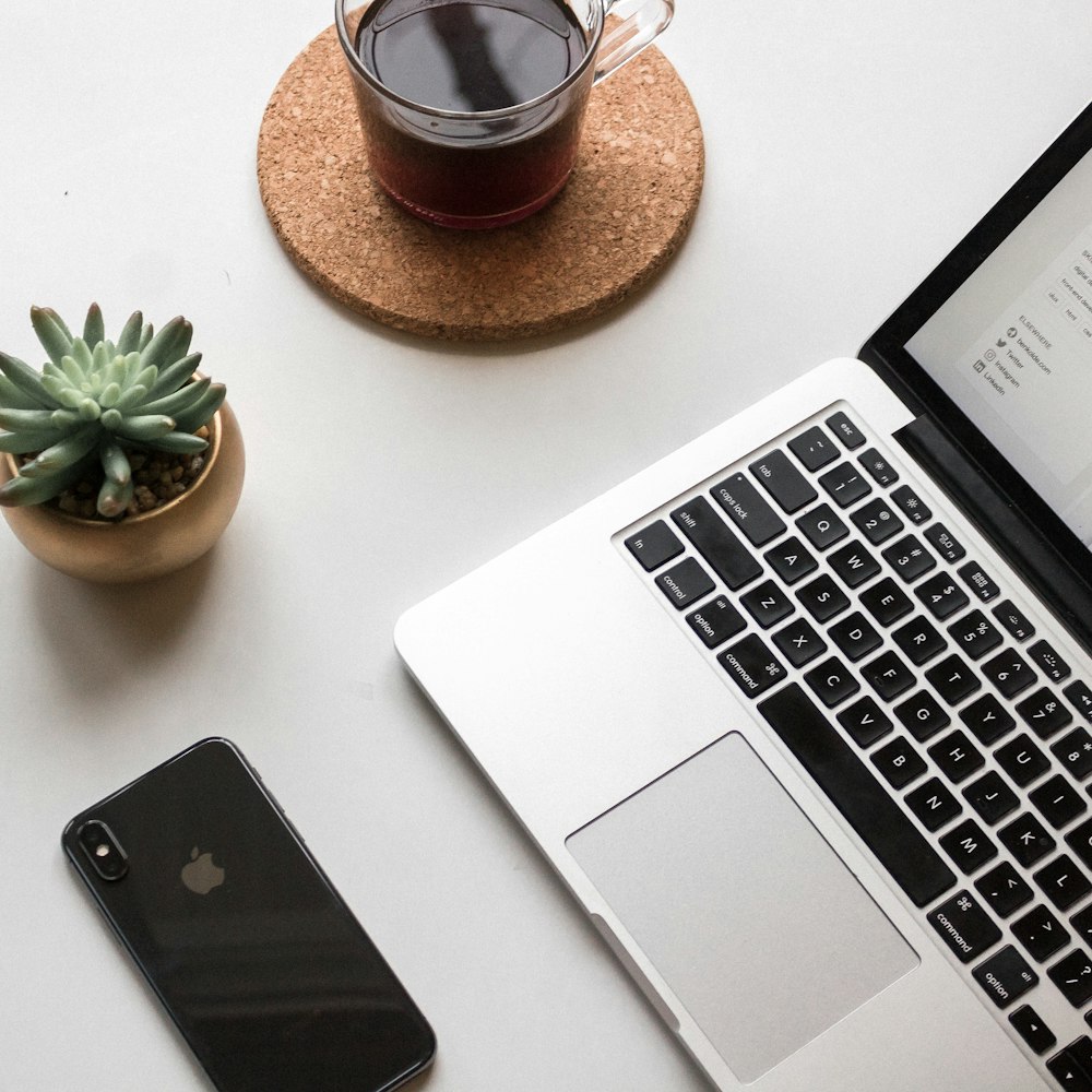 space gray iPhone X beside turned on laptop beside coffee and succulent plant