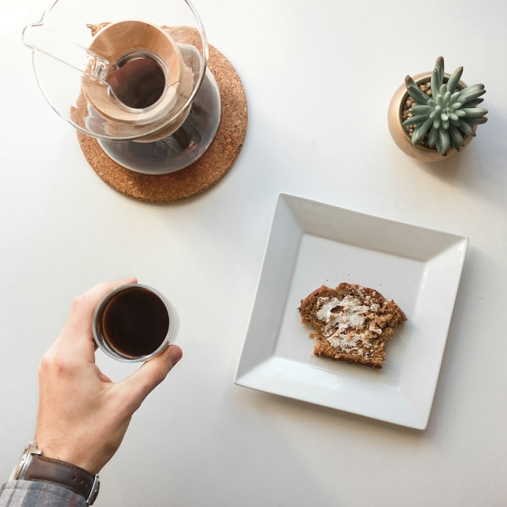 person holding cup of tea beside plate