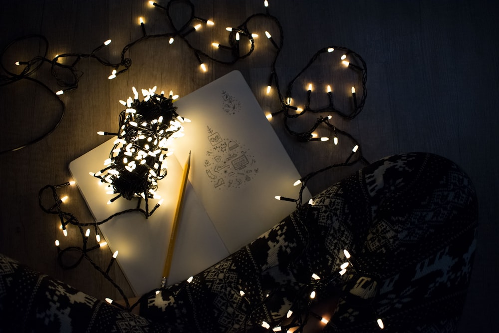 photo of string lights on open book beside pencil