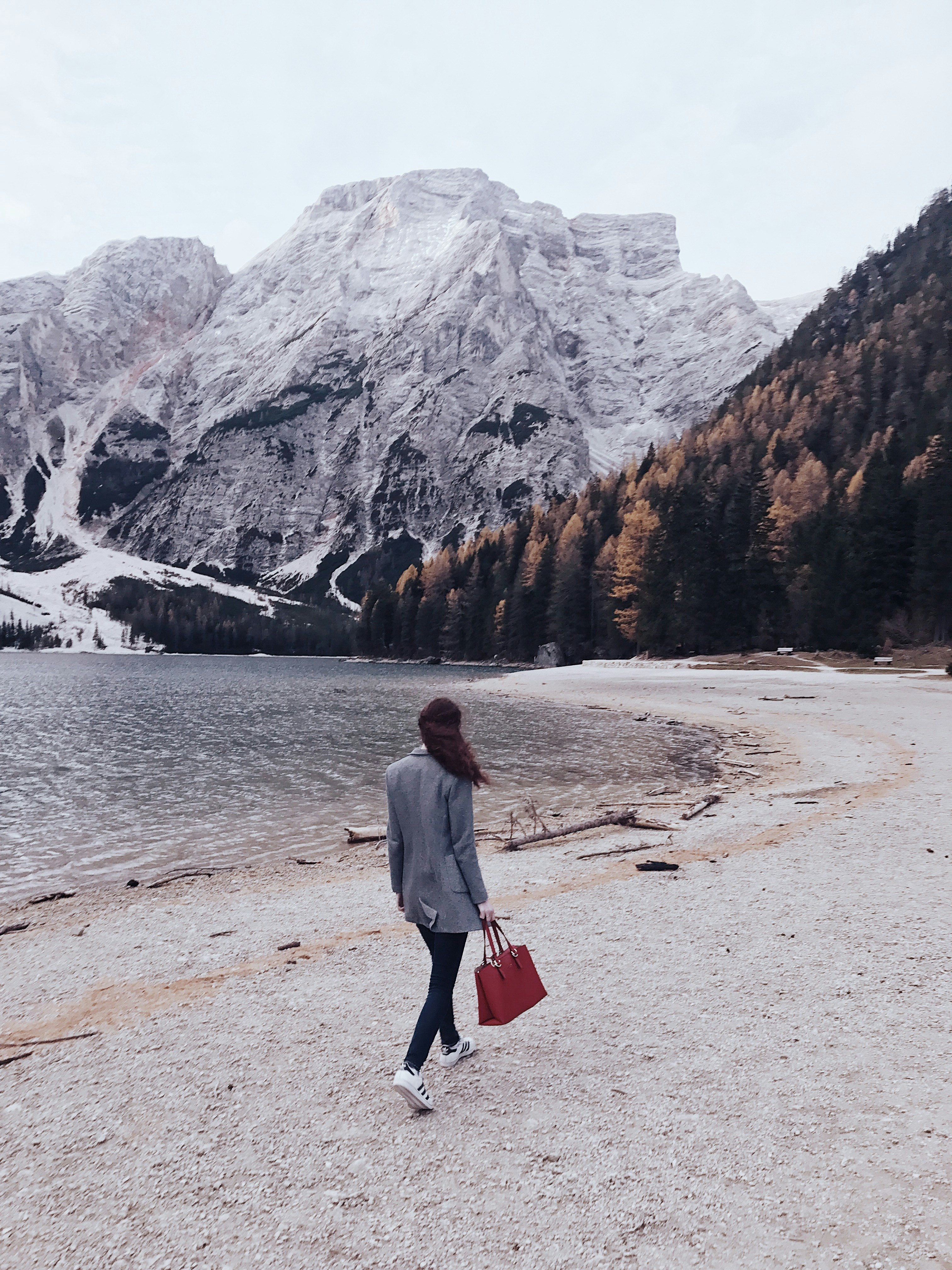 woman walking beside body of water toward snow covered mountain during daytime