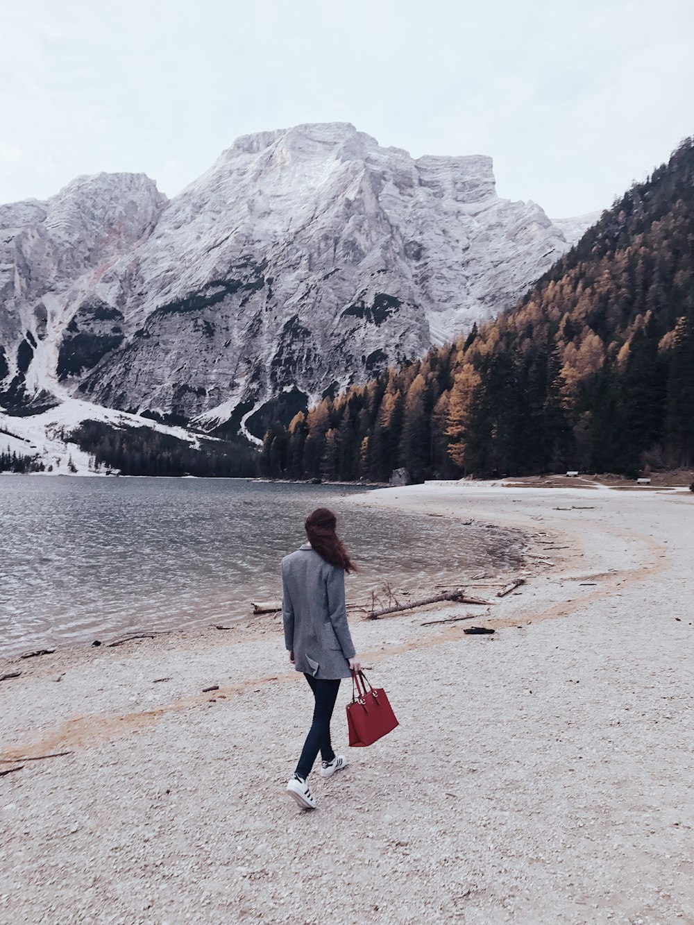 woman walking beside body of water toward snow covered mountain during daytime