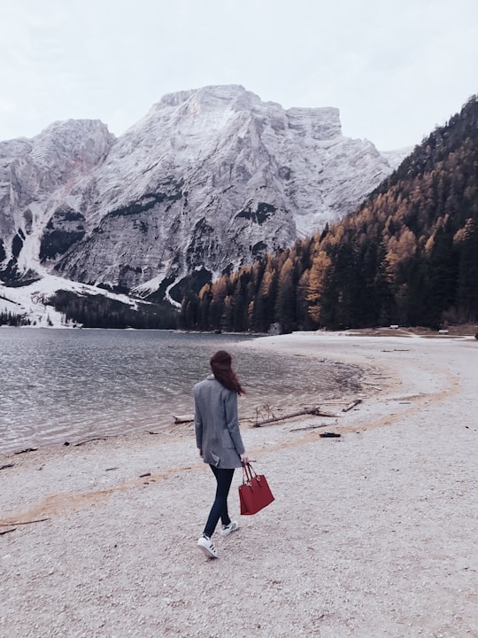 woman walking beside body of water toward snow covered mountain during daytime in Parco naturale di Fanes-Sennes-Braies Italy