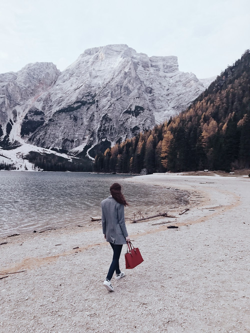 Mujer caminando junto al cuerpo de agua hacia la montaña cubierta de nieve durante el día