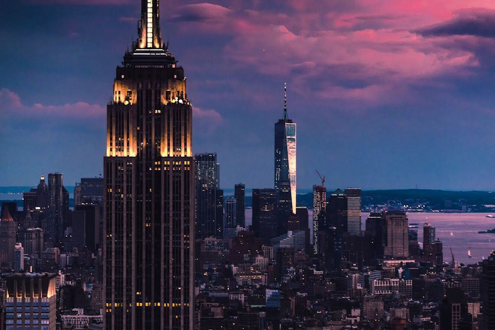 Empire State building surrounded by concrete buildings under cloudy sky