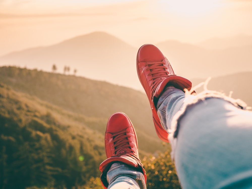 person in blue denim jeans and red low-top sneakers sitting on cliff