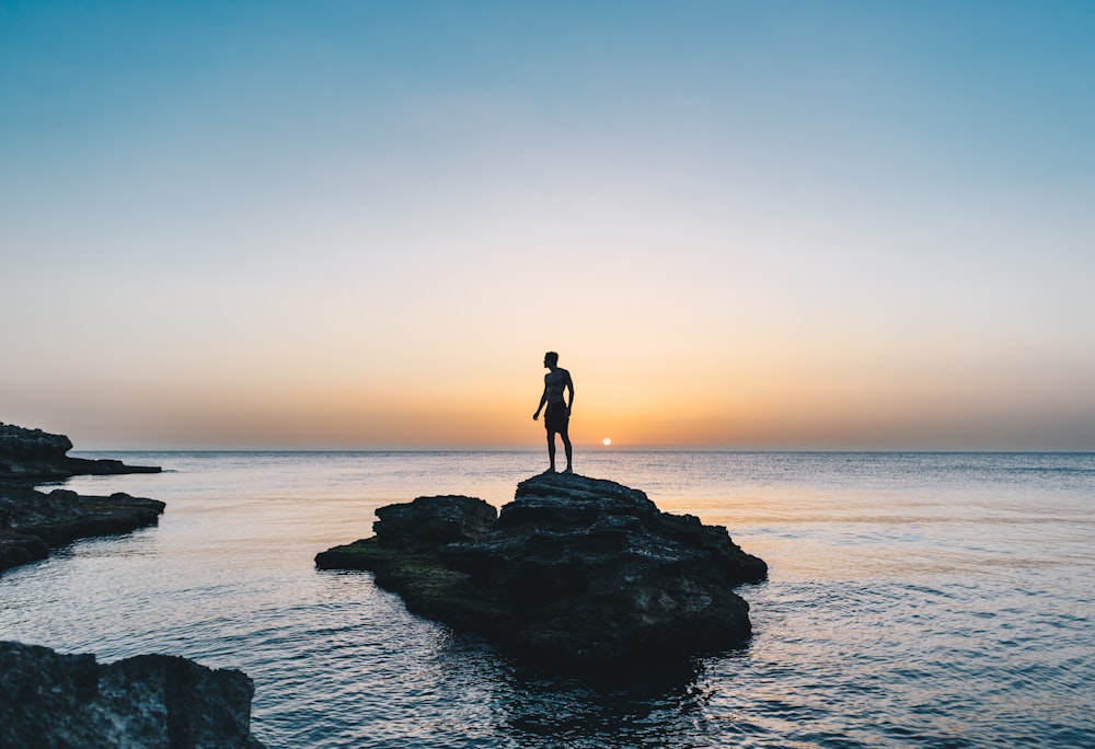 man standing on rock surrounded by body of water