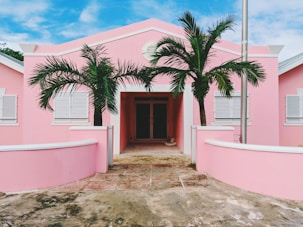 pink and white concrete house near green trees under cloudy sky