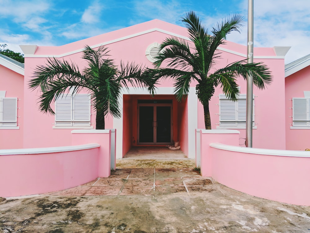 Maison en béton rose et blanc près d’arbres verts sous un ciel nuageux