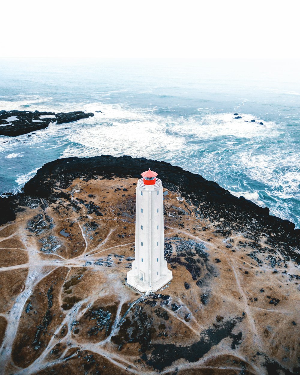 Fotografie aus der Vogelperspektive des weißen Leuchtturms in der Nähe des Ozeans