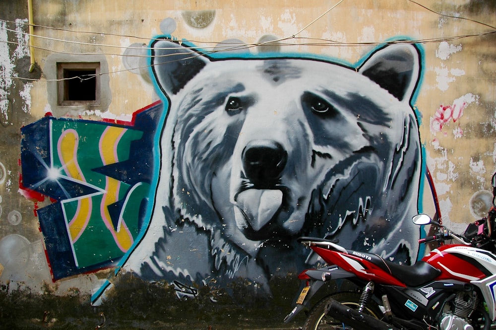 red motorcycle park next to wall with bear painting