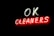 Neon sign displaying the words 'OK CLEANERS' with 'OK' in white and 'CLEANERS' in red letters, glowing brightly against a dark background.