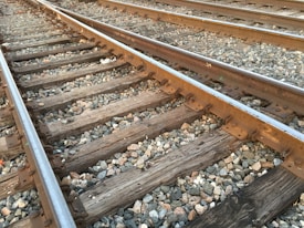 Metal train tracks laid out over wooden sleepers with rocks and gravel filling the spaces between the tracks. The tracks are parallel and appear to stretch into the distance.