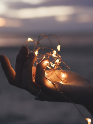 selective focus photography of person holding lighted brown string light