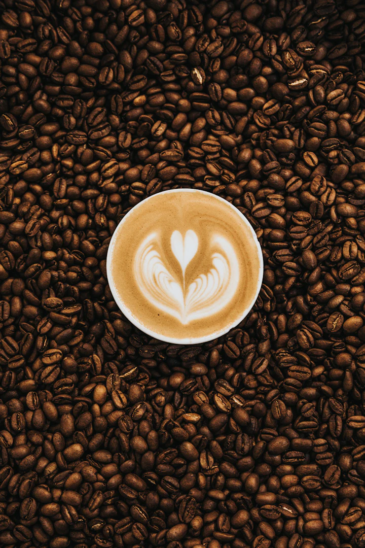 A cup of latte art resting on a bed of roasted coffee beans