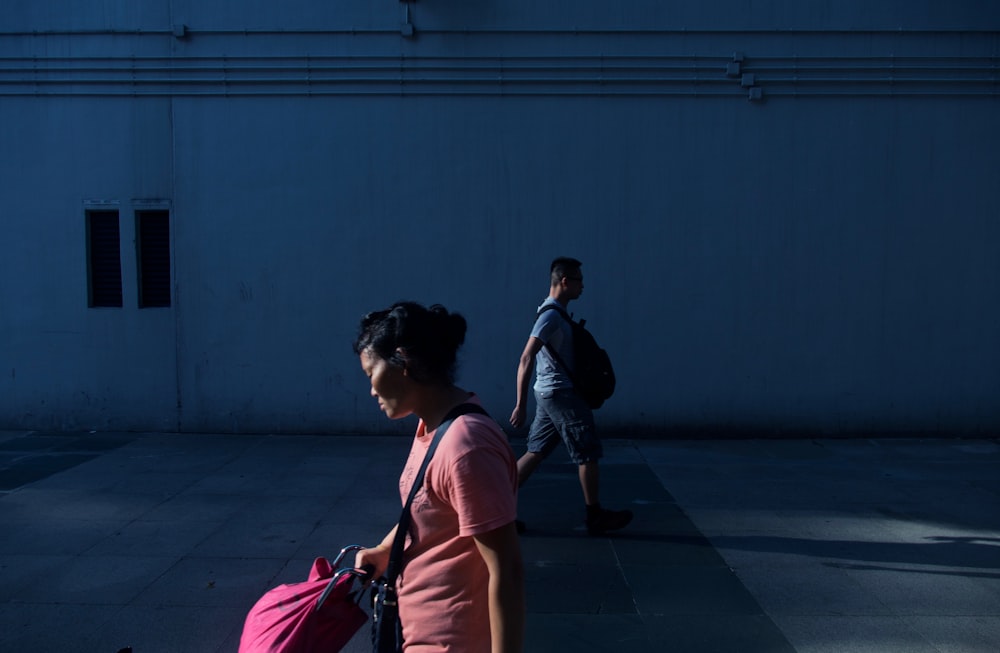 woman walking near man beside white wall at daytime