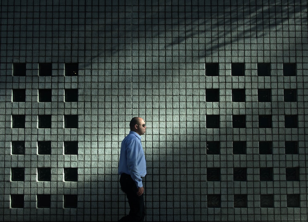 man in blue dress shirt walking near gray concrete wall