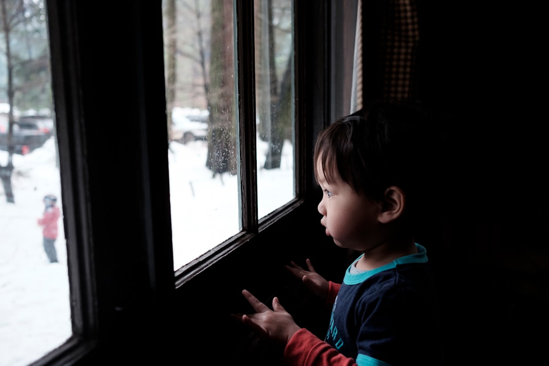 toddler boy standing near window during daytime