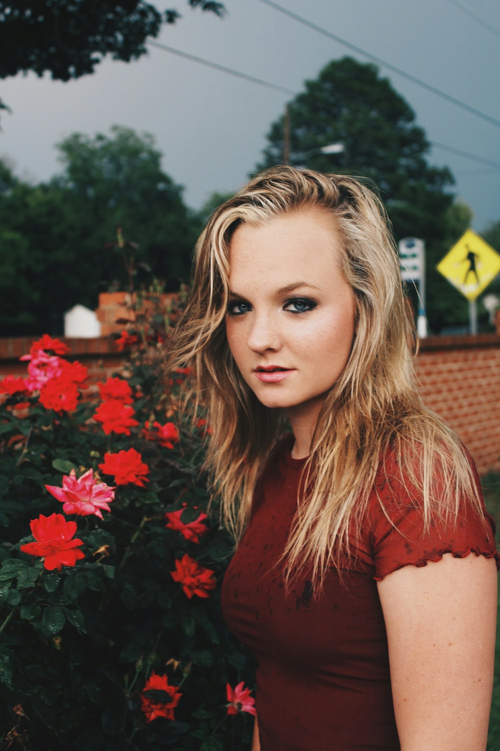 woman wearing red shirt standing near red petaled flower