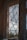 An intricately designed lace curtain partially obscures the view outside. The window reveals a cloudy sky and distant greenery, creating a soft barrier between the interior and the outside world. The curtain pattern features floral and curly motifs, giving a vintage feel.