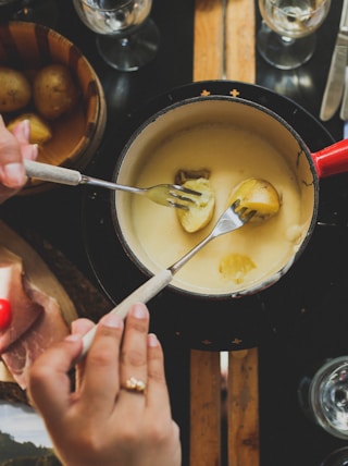 two person holding fork dipping food on sauce