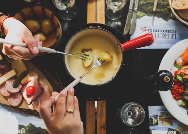 two person holding fork dipping food on sauce