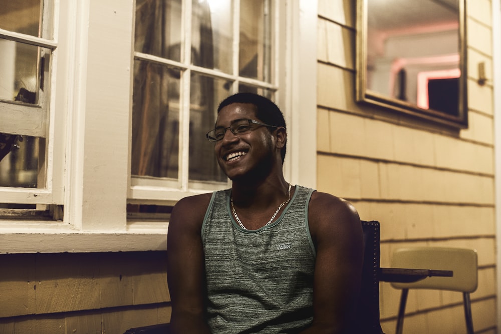 man in gray tank top sitting on wooden chair near window