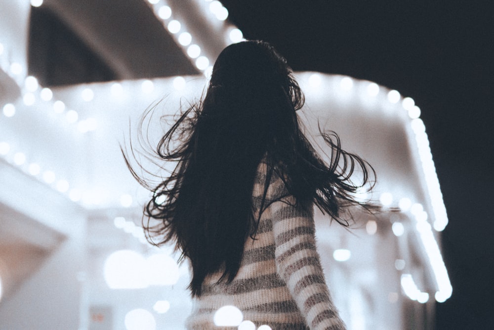 Photographie à mise au point peu profonde d’une femme faisant face à une structure en béton blanc pendant la nuit