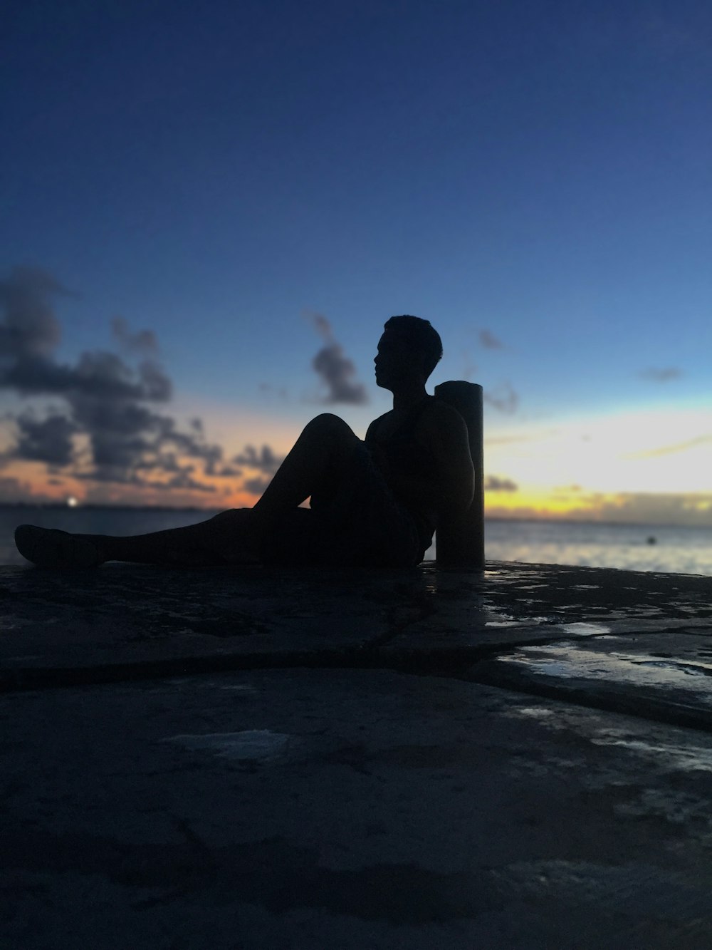 silhouette of man sitting on bay during susnet